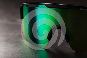 Sports glasses with a green mirrored lens and black frames on a black background