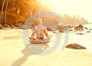 Sports guy at sunset practicing yoga in the sun and among tropic