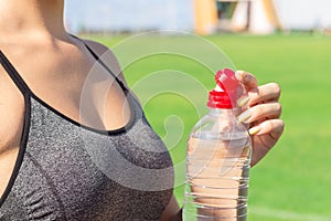 Sports and healthy concept. woman athlete is opening plastic bottle to drink water after training in stadium