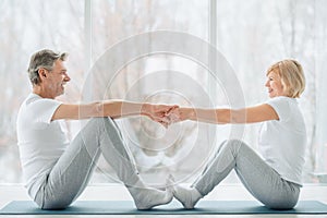 Sports and healthy lifestyle.Sporty middle aged couple sitting on the mat in the white fitness gym and doing stretching while