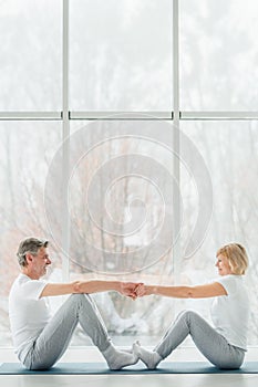 Sports and healthy lifestyle.Sporty middle aged couple sitting on the mat in the white fitness gym and doing stretching while
