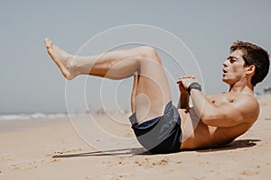 Sports and healthy lifestyle. Young man doing crunches on the ocean beach.