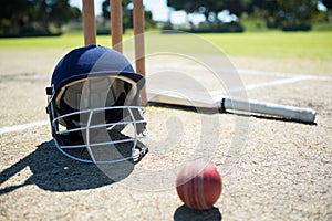 Sports helmet and ball with bat by stumps on pitch