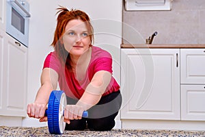 Sports at home in the kitchen, fitness during isolation due to coronavirus. A red-haired woman trains to strengthen the abdominal