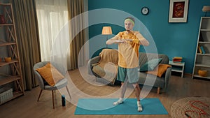 Sports at home. A man in sportswear and with a green headband is warming up in the living room. The man holds his arms
