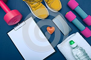 Sports at home - yellow sneakers, dumbbells and a bottle of water and a towel lie and a sheet of paper for sapisy achievements