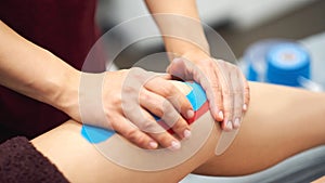 Sports injury kinesio treatment. therapist placing kinesio tape on patient`s knee