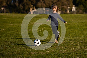 Sports kid during soccer training. Soccer boy, child play football. Kid kicking a football ball on a grass.