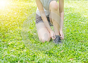 Sports Legs of young woman in fitness wear trying the shoestrings on green grass in the park. Healthy lifestyle concept