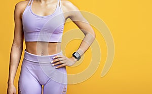 Sports lifestyle concept. Young fit woman in sportswear with fitness tracker posing over yellow background, free space