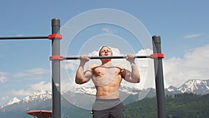 Sports man doing pull-up exercise on a horizontal bar against a blue sky.