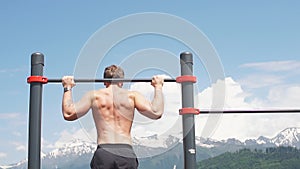 Sports man doing pull-up exercise on a horizontal bar against a blue sky.