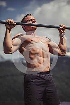 Sports man doing pull-up exercise on a horizontal bar against a blue sky.