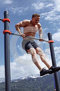 Sports man doing pull-up exercise on a horizontal bar against a blue sky.