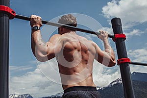 Sports man doing pull-up exercise on a horizontal bar against a blue sky.