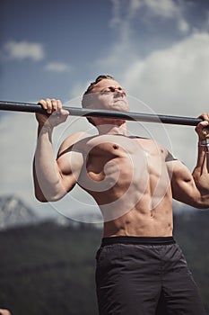 Sports man doing pull-up exercise on a horizontal bar against a blue sky.