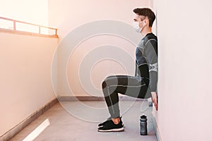 Sports man in face mask doing leg exercises at home