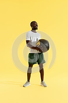 Sports man in sports wear with med ball on yellow background
