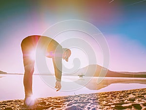 Sports man stretching bend back on beach. Runner exercising at lake