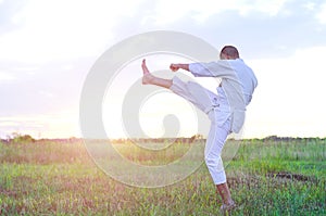 A sports man is training martial arts karate at sunset, a beautiful landscape with a copy space.