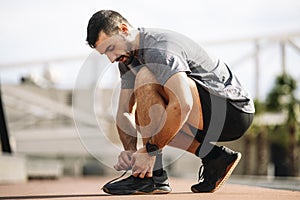 Sports man tying shoe laces in preparation for running training. Handsome young male getting ready to workout.