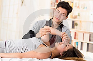 Sports massage. Hnadsome massage therapist massaging elbow of a female athlete, in a doctor office background