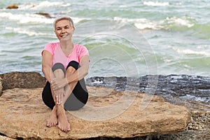 Sports mature woman sitting at the beach and smiling