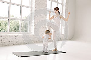 Sports mother is engaged in fitness and yoga with her baby at fitness or yoga studio. Young sporty woman doing standing