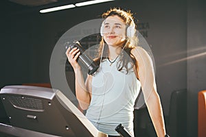 Sports nutrition and exercise. beautiful woman holds protein in her hand in bottles, shaker, listens music in headphones on head i