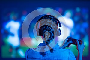 Sports online computer and video games among gamers. Girl with headphones and controller in front of a large TV screen. Sport game