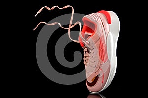 Sports pink sneakers on a black isolated background with soaring lacas in air, youth sports shoes, floating laces in the air