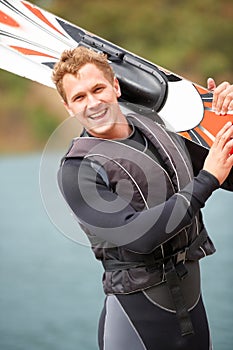 Sports, portrait and man by water with wakeboard for surfing, exercise and recreation hobby by lake. Fitness, extreme