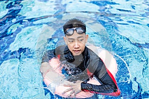 Sports and recreation concept a male adolescent wearing goggles and red and black swimming suit floating with a pool ring in the