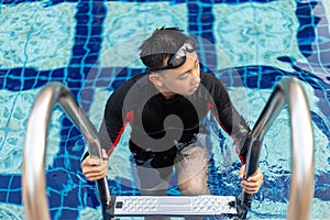 Sports and recreation concept a male adolescent wearing goggles and red and black swimming suit going out of the pool after