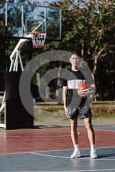 Sports and recreation concept a young male basketball player holding a basketball alone in the basketball court background