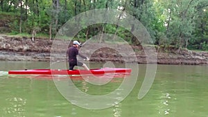 Sports rowing on the kayak. The man floats down the river along the wood.