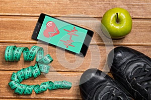 Sports shoes , Apple , measuring tape and a phone with health card on a wooden background. Mobile app health sensor for measuring