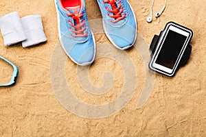 Sports shoes, earphones, smartphone against sand, studio shot.