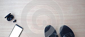Sports shoes with smartphone and headphones on wooden table photo