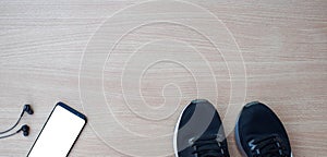 Sports shoes with smartphone and headphones on wooden table photo