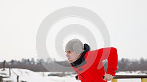 A sports trained man performs push-ups on parallel bars in the winter in the open air. Side view Slow motion. 120 frames