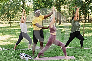 Sports trainer assisting group of senior women enjoying yoga outdoors in park