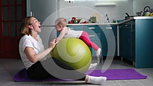Sports training at home. A young mother does exercises with a fitball and rolls her child on the ball. The concept of sports train