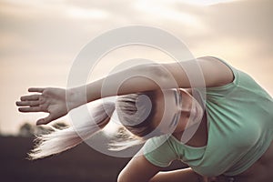 Sports woman exercises and stretches muscles on background of cloudy sky, girl engaged in fitness training outdoors, concept
