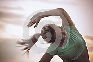 Sports woman exercises and stretches muscles on background of cloudy sky, girl engaged in fitness training outdoors, concept