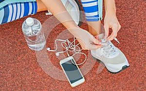 Sports woman runner tying shoelaces. Woman lacing her sneakers on a stadium running track