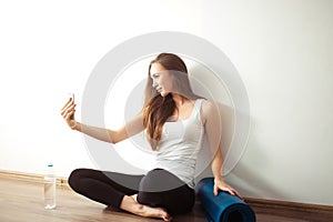 Woman sitting on floor and making selfie on smartphone in fitness gym