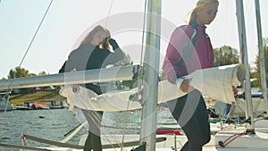 A sports yacht team of girls takes a folded sail from the hold of the yacht to set it on the mast.