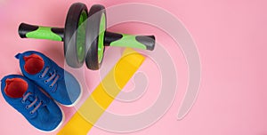 Sports yellow elastic band . Sports equipment. Yellow elastic band on a pink background. Green dumbbell. Sports sneakers. Training