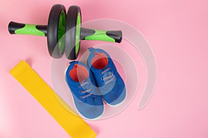 Sports yellow elastic band . Sports equipment. Yellow elastic band on a pink background. Green dumbbell. Sports sneakers. Training